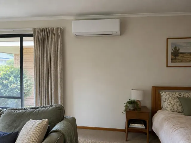 Wall-mounted split system in a living room with curtains, sofa and bedside table in Highbury